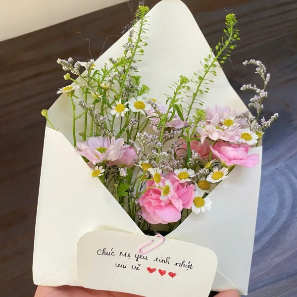 A bouquet of pink and white flowers in a cream envelope, with a handwritten card.