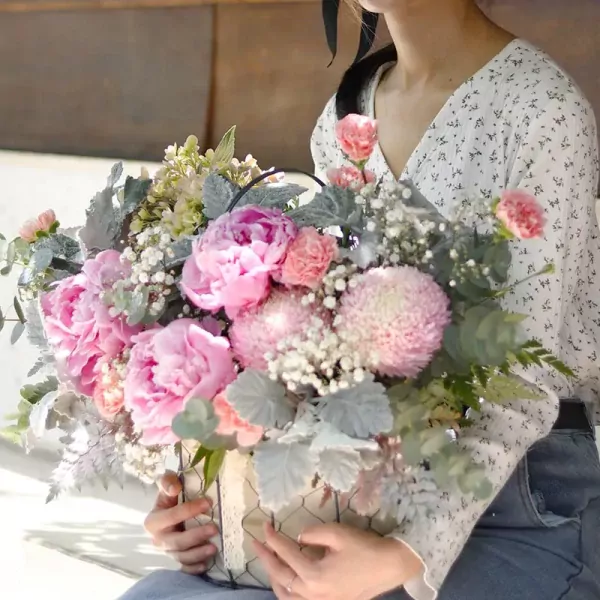 Pink peonies, carnations, and chrysanthemum bouquet in a wire basket.