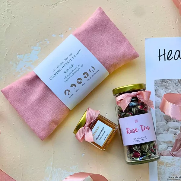 Pink herbal pillow, rose tea jar, and mini honey with pink ribbon bows on a pastel background.