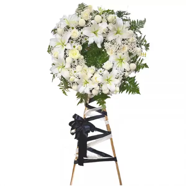 White funeral wreath with lilies, roses, and carnations on a wooden easel with black and white ribbons.