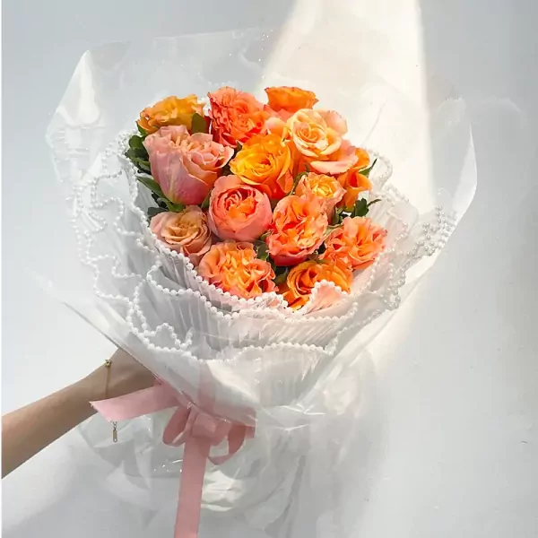 Bouquet of orange and pink roses with white lace and pink ribbon.