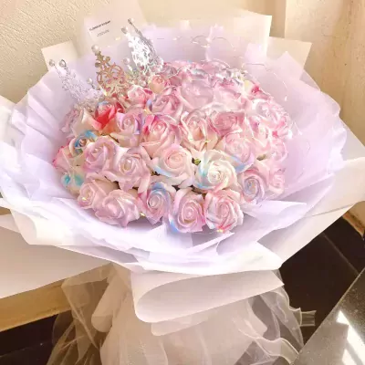 Rainbow gradient roses in a white bouquet with a silver crown.
