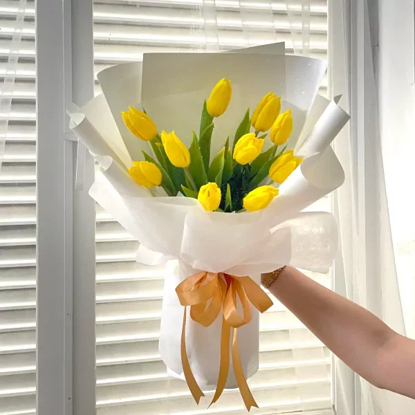 Bouquet of 10 yellow tulips wrapped in white paper, tied with a golden ribbon.