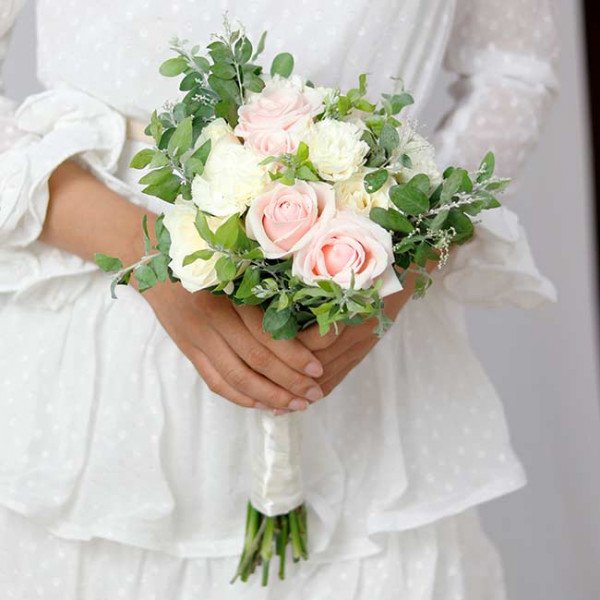Bride holding a pastel pink and white rose bouquet with greenery.