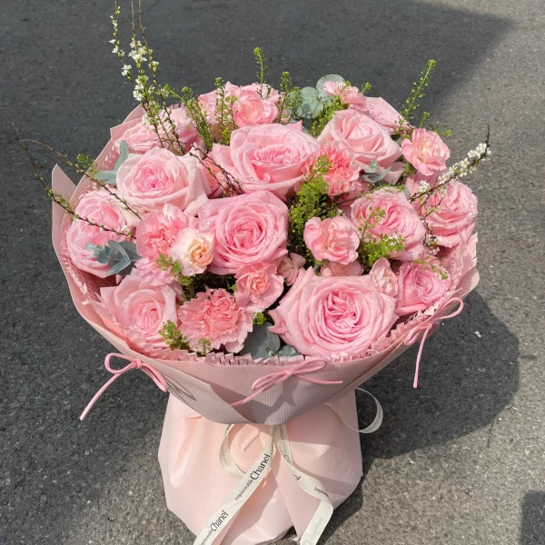 A pink rose bouquet with carnations, wrapped in pink paper and tied with a ribbon.