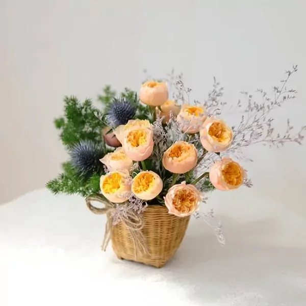 Basket of peach David Austin roses and blue thistles, tied with twine.