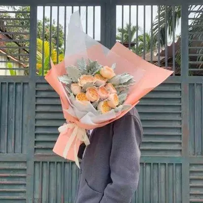 Peach and pink rose bouquet with greenery, held by a person with their face obscured.