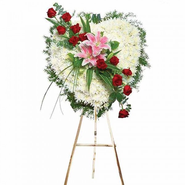 Heart-shaped funeral wreath with white chrysanthemums, red roses, and pink lilies on a wooden easel.