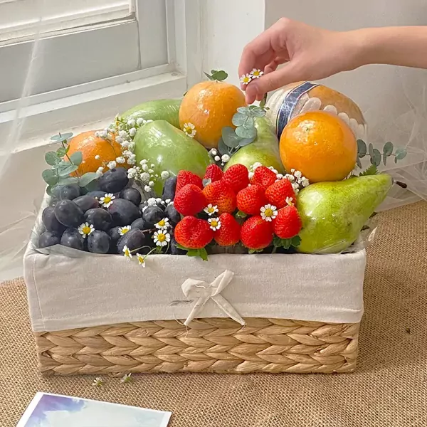 A fruit basket filled with oranges, pears, strawberries, and grapes, decorated with small white flowers.