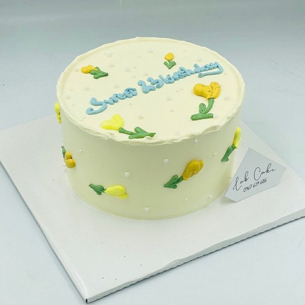 Yellow cake with blue "Sweet Birthday" lettering and yellow tulip decorations.