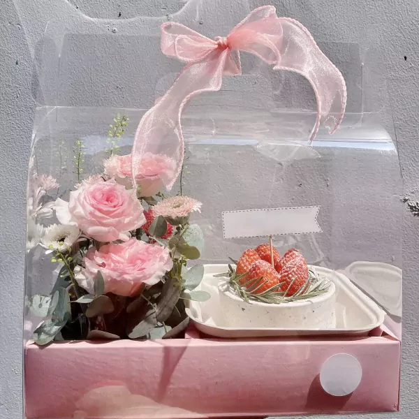 Pink roses, flowers, and a cake with strawberries in a clear box.