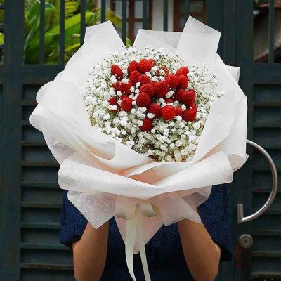 Bouquet of white baby's breath and red raspberries in white paper wrapping.
