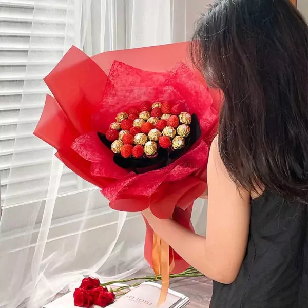 Chocolate and strawberry bouquet with red wrapping and ribbon held by a person.
