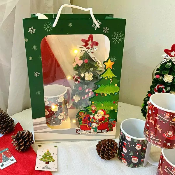 Christmas gift set with mugs, miniature tree, and festive decorations in a green box.