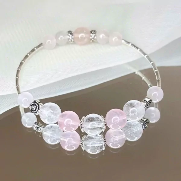 A bracelet with pink and clear beads and silver charms on a white fabric.