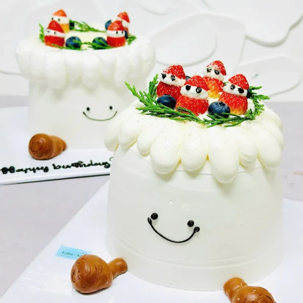 Cute Christmas cake with strawberry snowmen, blueberries, and a smiling face design.