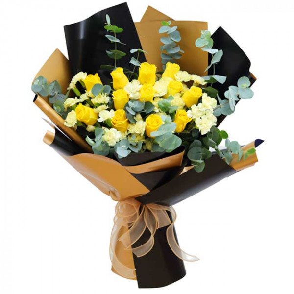 Yellow roses, carnations, and eucalyptus in a black and gold bouquet with a ribbon.