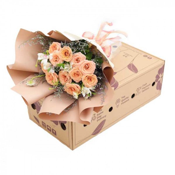 Peach roses and white flowers in a bouquet on a cardboard box.