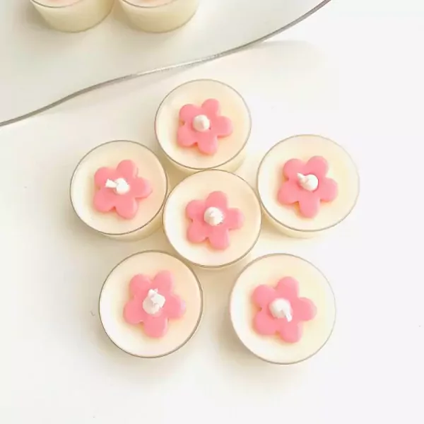 Six tea lights with pink flower decorations on a white background, with a silver wire in the upper left.