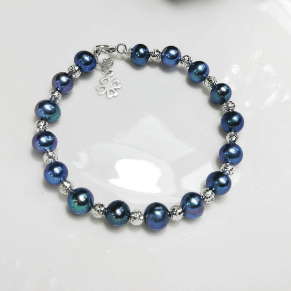 A dark blue pearl bracelet with silver accents and a clover charm.