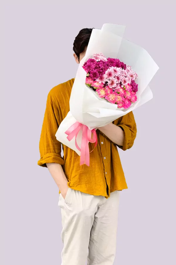 Person holding a pink and purple floral bouquet with white paper wrapping and pink ribbon.