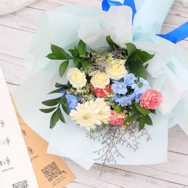 A bouquet of white, yellow, blue, and pink flowers with green leaves, wrapped in light blue paper.