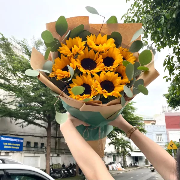 Bouquet of bright sunflowers with eucalyptus leaves, wrapped in brown and green paper.