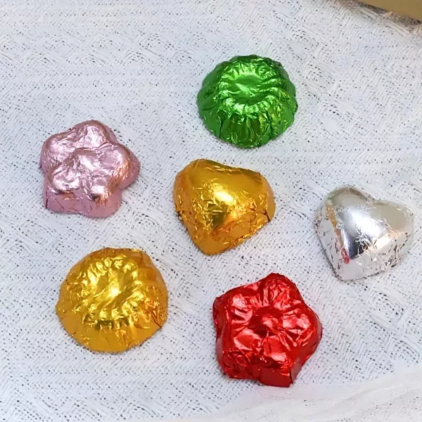 Chocolates in colorful foil wrappers, including heart shapes, on a textured white surface.