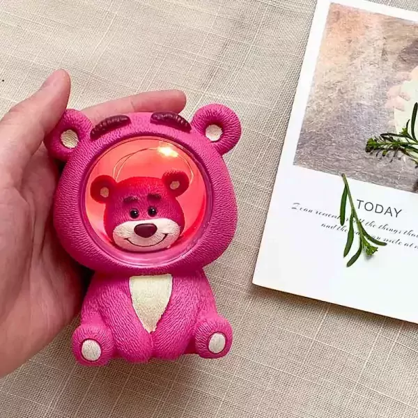 Pink Lotso bear night light with red lights inside, held by a hand.