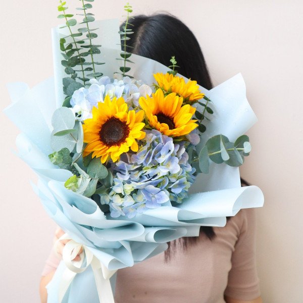 A bouquet of sunflowers and hydrangeas in light blue paper wrap.