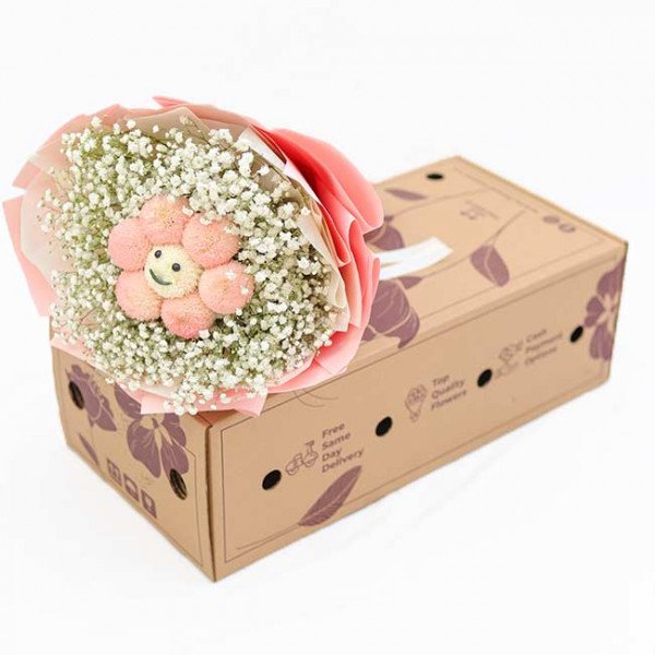 A flower bouquet with a smiling pink flower and baby's breath sits on a delivery box.