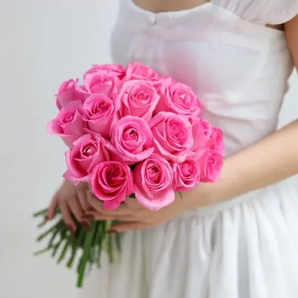 A bride holds a bouquet of 20 bright pink roses.