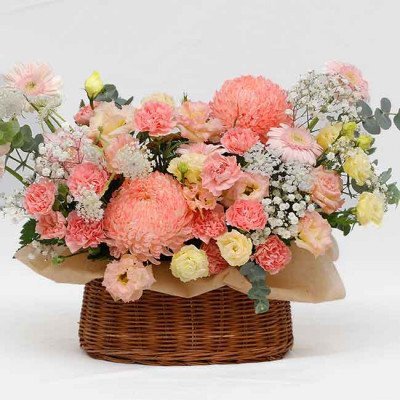 Pink and peach floral arrangement in a brown wicker basket with a light brown paper liner.