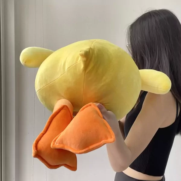 A person holds a large, soft yellow duck plush toy with orange feet.