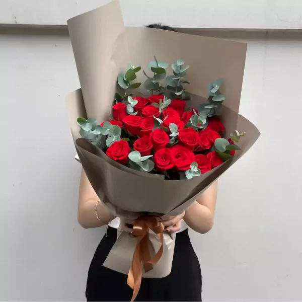 Bouquet of red roses with eucalyptus leaves, wrapped in brown paper and tied with a ribbon.