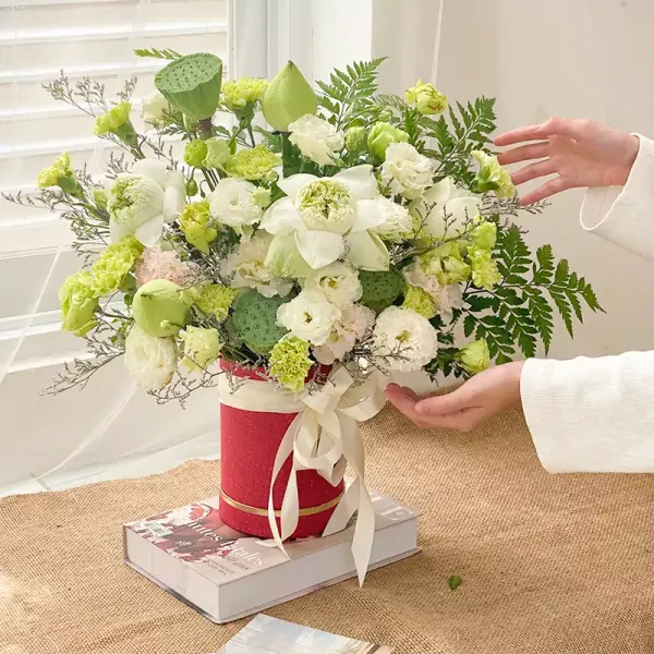 Bouquet of white lotuses, green carnations, and lisianthus in a red box.