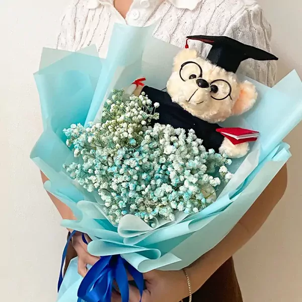 Graduation bouquet with a teddy bear in a cap and gown surrounded by baby's breath flowers.