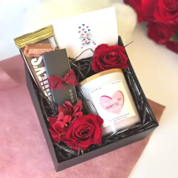 Valentine's gift box with a chocolate bar, scented candle, and red roses.
