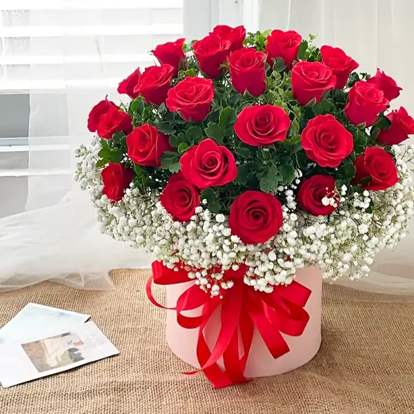 A hat box of red roses and baby's breath with a red ribbon.