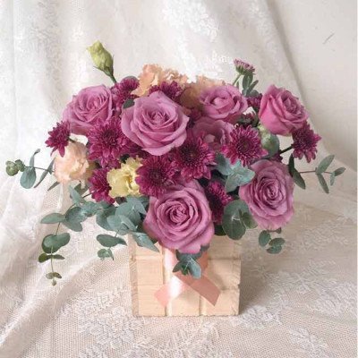 Box of purple roses, carnations, and chrysanthemums with eucalyptus leaves.