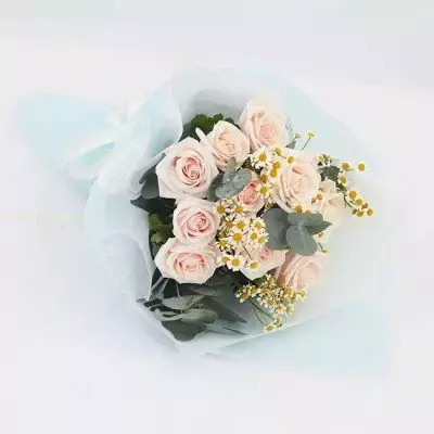 Bouquet of pale pink roses, daisies, and eucalyptus leaves wrapped in light blue paper.