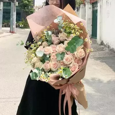 Bouquet of pink roses, white flowers, and eucalyptus leaves, wrapped in brown and pink paper.