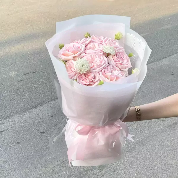 Bouquet of pink roses with white filler flowers, wrapped in white and pink paper, tied with a pink ribbon.