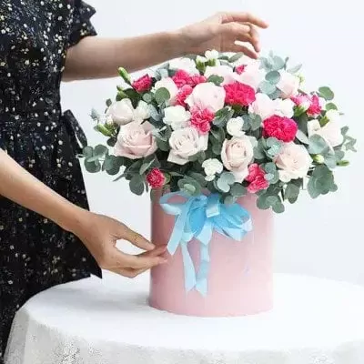 Pink box of roses, carnations, and eucalyptus, tied with a blue ribbon.