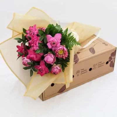 Pink lotus flowers in a bouquet wrapped in sheer gold fabric on a cardboard box.