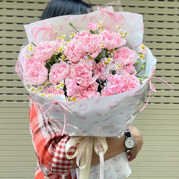 Pink carnation bouquet with Hello Kitty paper wrap held by a person wearing a red and white plaid shirt.