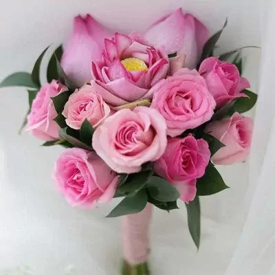 Pink lotus and rose bridal bouquet with green leaves and pink ribbon wrap.