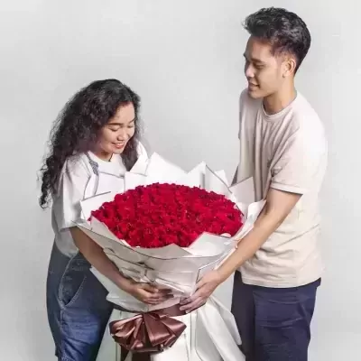 Couple holding a giant bouquet of 200 red roses.