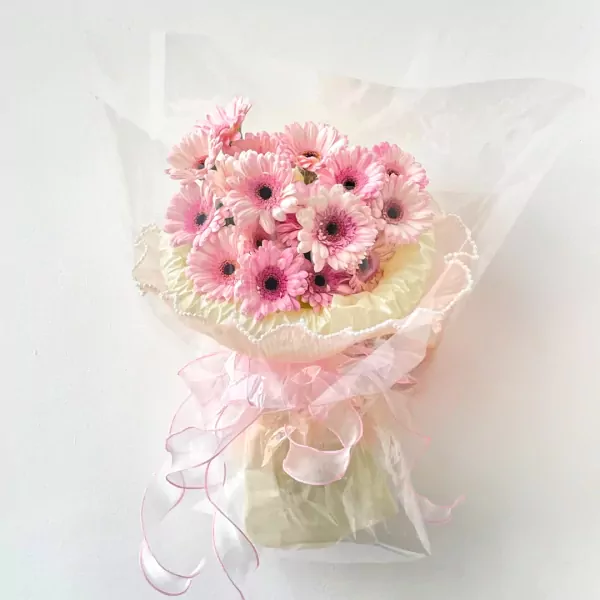 Pink gerbera daisy bouquet with sheer pink and yellow wrapping and ribbon.