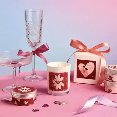 Valentine's gift set with candles, glasses, and gift box tied with ribbons on a pink surface.